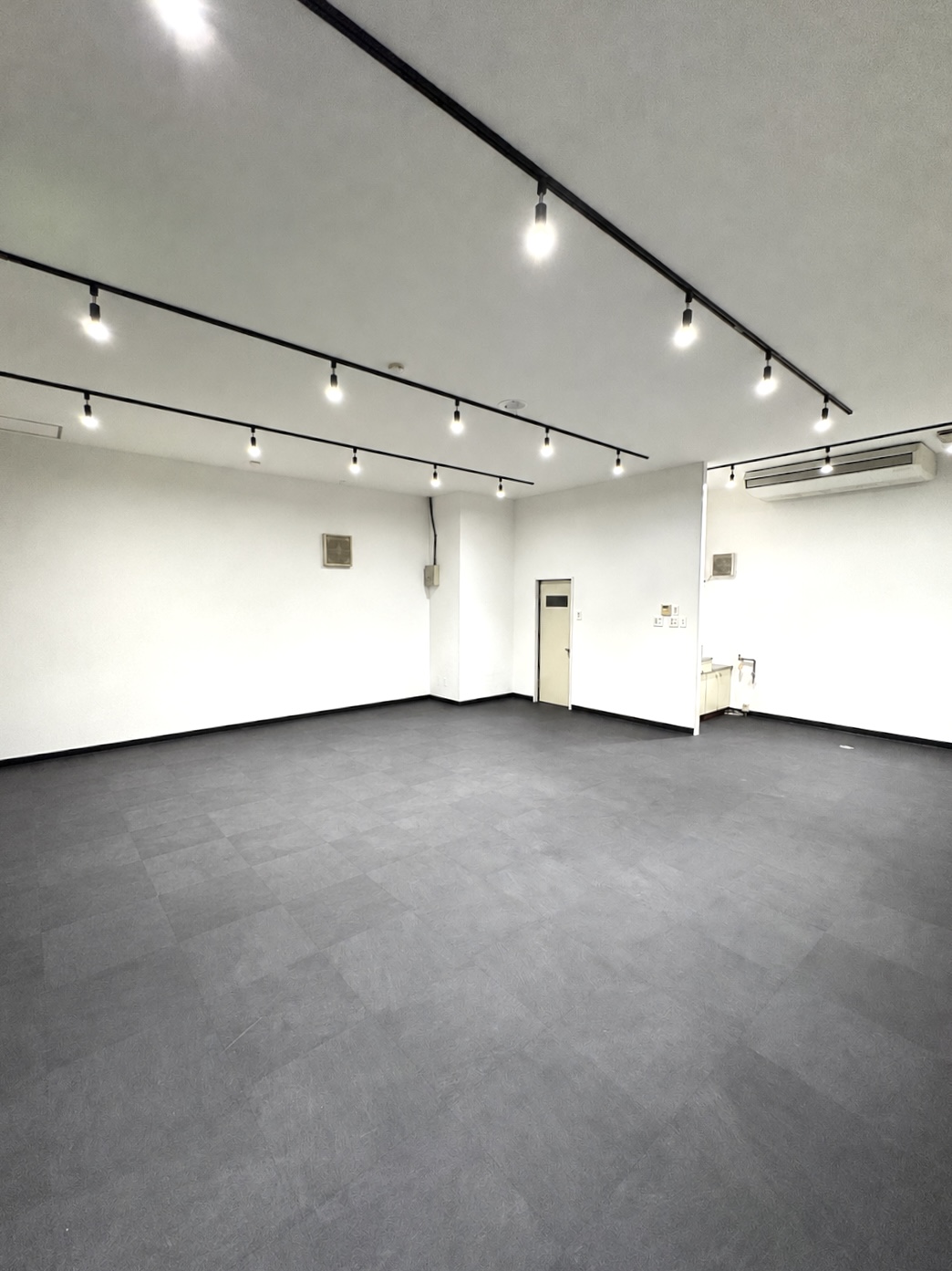 LUKE Body Fitness与那原店の店内。白い壁と黒い床、天井のレール照明があるトレーニングスペース。